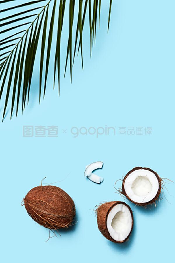 一片椰子和整個椰子,在藍色背景上有一片棕櫚綠葉。食物成分。平鋪。一個由有機的一半和一個椰子組成的美麗組成的藍色背景裝飾著一塊飾板,上面有一片平鋪。